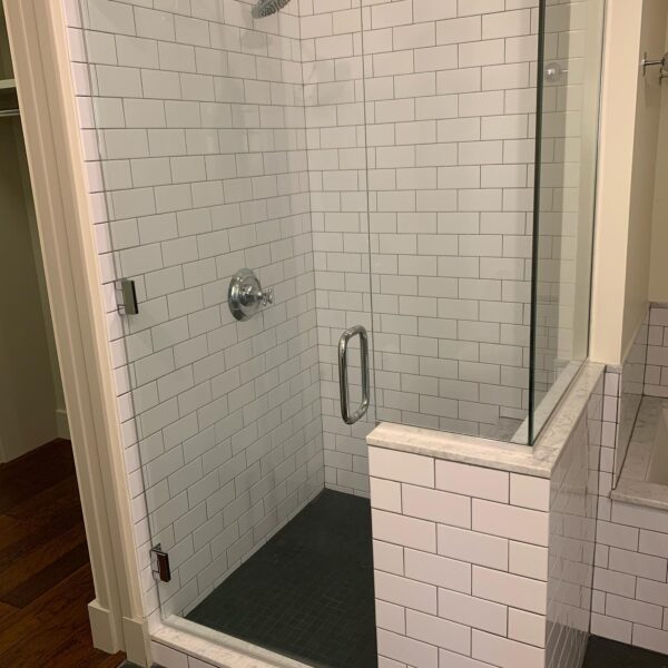 A shower with a glass door and tiled walls.