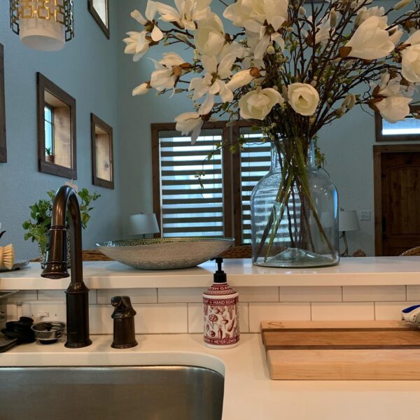 A bathroom with a sink, mirror and flowers in the vase.